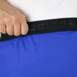 نمای نزدیک از کش کمر پهن با نوشته بافته‌شده adidas در شلوارک ورزشی آبی